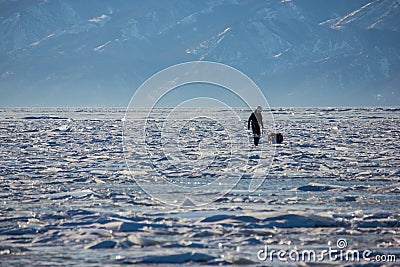 male hiker with backpack walking on ice water surface against peaks on shore,russia, lake Editorial Stock Photo